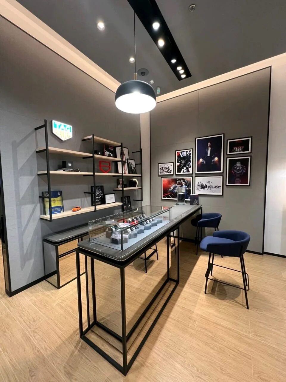 Tag Heuer display counter with glass case, a pendant light above, wall shelves and framed images under recessed spots