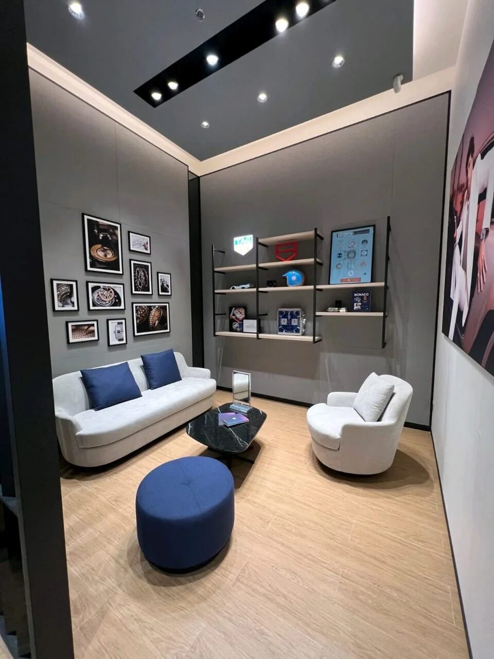 Lounge corner in the Tag Heuer store with a white sofa, blue cushions and a wall of framed photographs